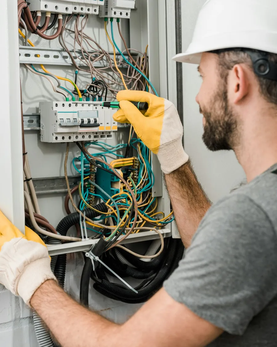 Electricista con casco y guantes trabajando con un destornillador en un cuadro eléctrico